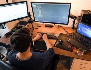 APA/AFP/INA FASSBENDER Mann sitzt an seinem Schreibtisch mit drei Monitoren