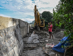 Ein Mann steht mit Kind in Armen neben einem unfertigen Damm in Plaridel in der Bulacan-Region, Philippinen