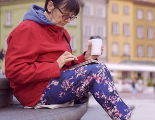 Frau sitzt an einem Brunnen mit einem Kaffee in der Hand und schaut auf ihre Smartphone
