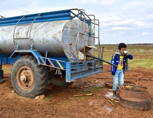 Kind trinkt Wasser von einem Wassertank in einem Camp