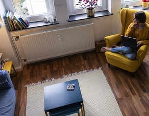 Person sitzt zuhause in einem gelben Armsessel und arbeitet am Laptop