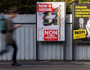 Eine Person geht an Plakaten der Kampagne „Nein zur Halbierung des SRG SSR“ vorbei. Die Slogans lauten: "Zerstörung des Zusammenhalts" und "Gegen die Volksinitiative 200 Franken sind genug"