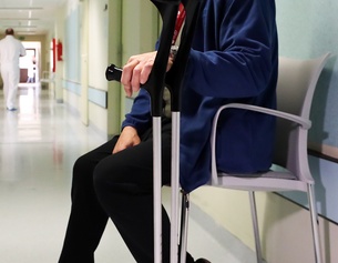 Mann nach einer Hüft-OP auf einer Bank sitzend mit Krücken, Krankenhaus