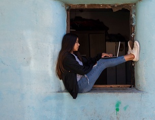 Mädchen mit Laptop in einem Fenster sitzend