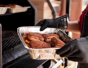 Eine Aluschale mit Grillgut wird bei einem BBQ-Bewerb gehalten