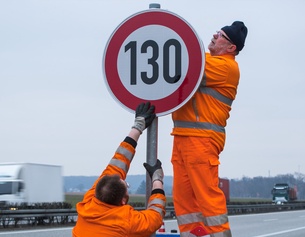 Zwei Männer montieren ein Schild auf der Autobahn mit der Ziffer 130.