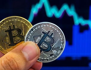 Ein Mann hält zwei Bitcoins in der Hand