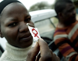 Eine Frau in Botswana hält eine Anstecknadel mit einem Aids Zeichen in die Kamera.