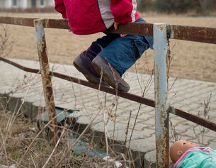 Kind sitzt auf Metallgeländer und Puppe auf dem Boden 