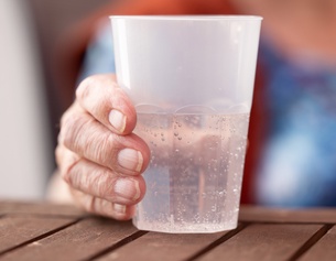 Die Hand einer alten Dame hält einen Plastikbecher mit Mineralwasser, Pflegeheim