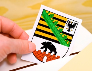 Hand wirft Landeswappen des deutschen Bundeslandes Sachsen-Anhalt in eine Wahlbox