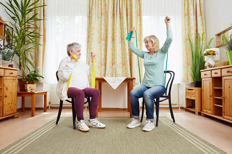 Ein Gesundheitsbuddy macht mit einer älteren Frau Übungen mit einem Theraband